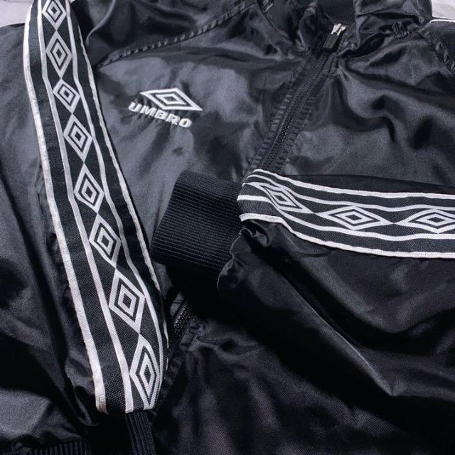 UMBRO(アンブロ)の90s umbro ナイロン トラックジャケット 黒 L ロゴテープ デサント製 メンズのジャケット/アウター(ナイロンジャケット)の商品写真